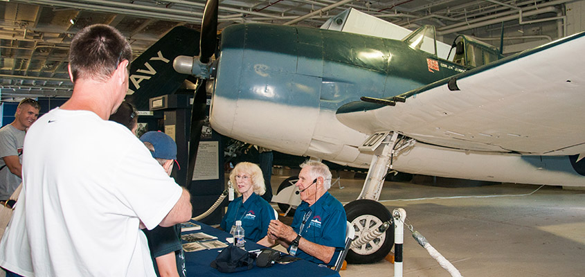 Fighter pilot Lt. Bill Watkinson flew the same aircraft Vice Admiral James Flatley Jr. did in WWII. Here he sits with Connie Reynolds answering questions in the USS Yorktown hanger. © 2016 Audra L. Gibson.